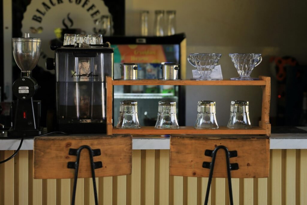 Cozy coffee shop counter with brewing equipment and wooden chairs.