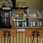 Cozy coffee shop counter with brewing equipment and wooden chairs.
