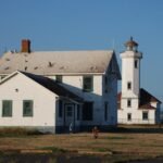 Historic Point Wilson Lighthouse and adjacent building in Port Townsend, WA, under clear blue sky.